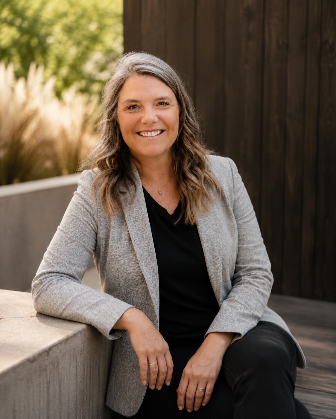 Amee Hardy, LCPC &mdash; portrait, seated on a concrete bench with ornamental grasses behind